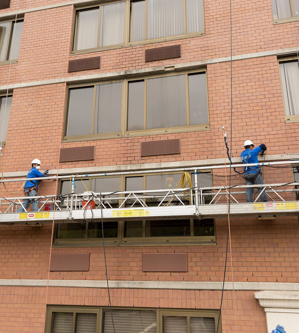 Workers cleaning brick on the side of a building