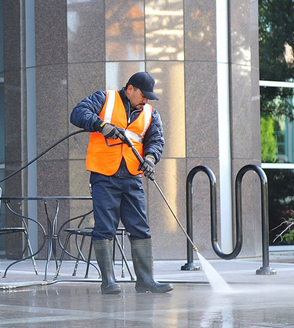 A worker pressure washing a sidewalk